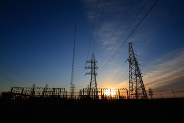 Many high-voltage power towers, silhouetted against the setting sun