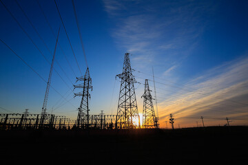 Many high-voltage power towers, silhouetted against the setting sun