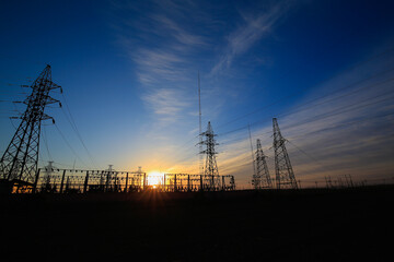 Many high-voltage power towers, silhouetted against the setting sun