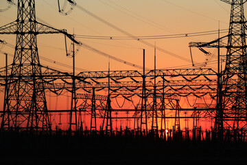 Many high-voltage power towers, silhouetted against the setting sun
