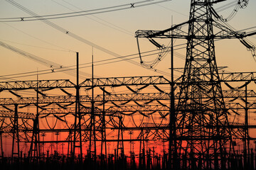 Many high-voltage power towers, silhouetted against the setting sun