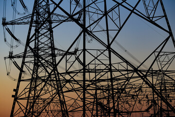Many high-voltage power towers, silhouetted against the setting sun
