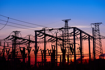Many high-voltage power towers, silhouetted against the setting sun