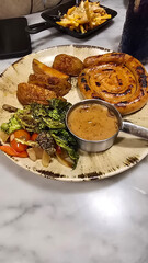 mouthwatering German worst curled up cumberland sausage meal featuring a grilled sausage, loaded cheese fries, and fresh vegetables served on a rustic plate