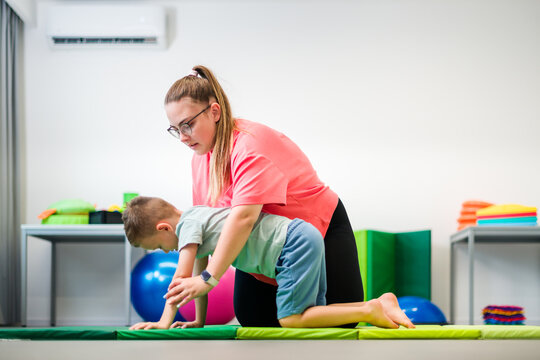 Young boy exercising with physical therapist during therapy session. Child physical therapy. Bilateral coordination.