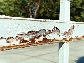 rusty metal fence with peeling paint and rust,  rusted metal fence with peeling paint, showing signs of wear and decay, background features blurred greenery and outdoor lighting.