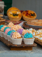 Muffins with pastel colored cream and cakes on the market counter