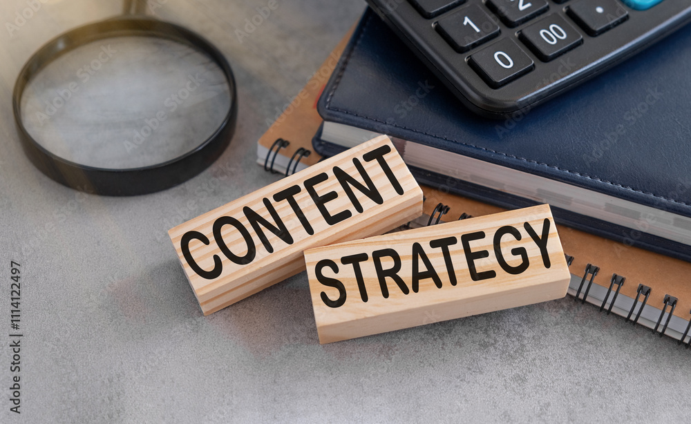 Poster content strategy text on wooden blocks on grey background with notebook and calculator.