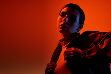 A fashionable young woman showcases her makeup and stylish attire while striking a pose in a studio.