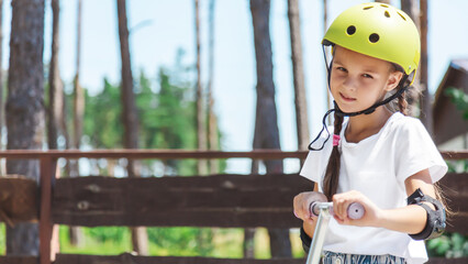 A little girl ride on a scooter in the park. Children's summer active recreation. Copy space.