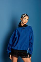 A young woman showcases trendy attire with hair clips against a bold blue backdrop