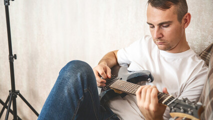 Musical hobby. Guitar skill. Man sitting on sofa playing string instrument enjoying learning chords...