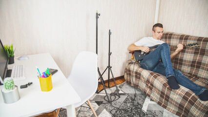 Musical hobby. Guitar skill. Man sitting on sofa playing string instrument enjoying learning chords...