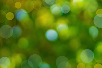 Blurred natural green background of tree foliage with round large blurred points of light in blue, yellow shade of bokeh effect. Abstract defocus background