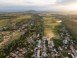Mountain landscape in summer at sunset. Green and yellow fields on the hills. Lake and village near...