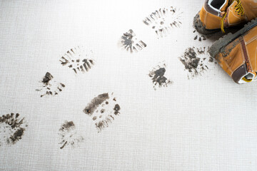 Wet muddy footprints on the carpet in the living room. A pair of brown boots on the background....