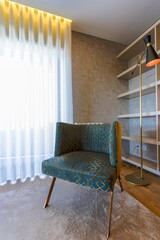 Modern green grey velour chair in home interior, shelves on the background