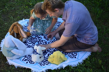 A young father spends quality time with his children outdoors in the backyard, engaging in a playful tea party with stuffed animals. The scene highlights family bonding, imagination, and joy.