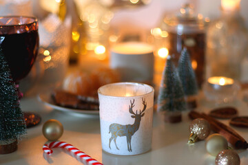 Various Christmas decorations, cookies, chocolate, nuts and tangerines, wine glasses and lit candles on the table. Holiday hygge at home. Selective focus.