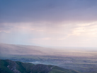 Drone view of mountains at sunset. A lot of clouds on the sky. The setting sun illuminates the valley, village and fields. Evening landscape.