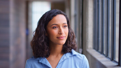 Head And Shoulders Portrait Of Confident Businesswoman Standing By Window In Modern Office