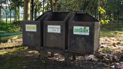 A rusty trash can in a park separated into three categories of waste, namely inorganic waste, B3 waste and organic waste