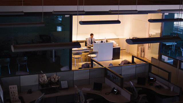 Wide Angle Shot Of Businessman At Desk Working Late At Night In Empty Office