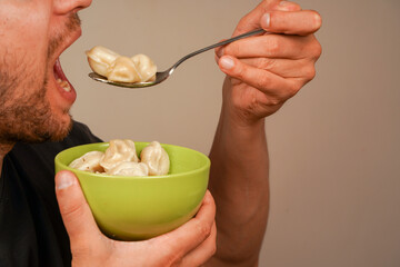 A tender dumpling, lifted on a spoon near an open mouth, demonstrates a personal dining moment. A...