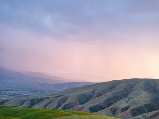 Drone view of mountains at sunset. A lot of clouds on the pink and blue sky. Evening landscape.