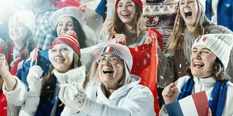Large group of French sports fans dressed in national colors, waving flags, and cheering during exciting sports game in winter stadium. Concept of sport, game, competition, emotions