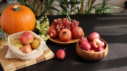  Pumpkin, pears, pomegranates, grapes, and apples arranged on dark table with greenery create vibrant autumn scene, emphasizing eco fruits and eco harvest concept for seasonal display.