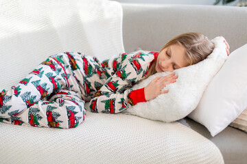 Girl sleeping on a cozy couch in festive pajamas. A young girl peacefully sleeping on a soft white...