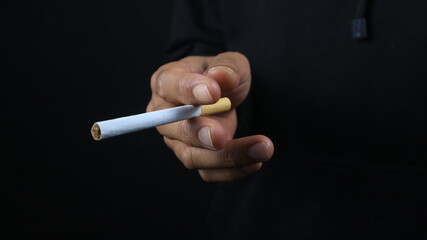 a man's hand holds a cigarette, black background