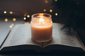 Burning candle and open Bible book with bokeh lights, Christmas background.