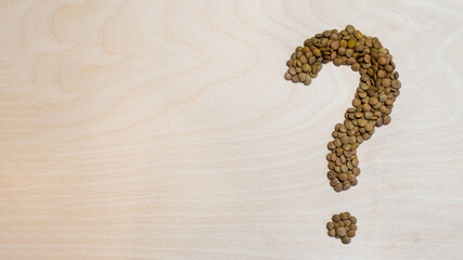 question mark made of green lentils on a wooden background with space for text. The concept of health care, eating healthy foods. Banner with free space for text