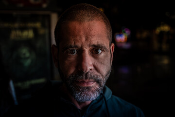 A man with a beard and a mustache is staring at the camera. He is wearing a black hoodie and he is in a serious or contemplative mood