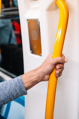 A person is holding a yellow pole on a train. The pole is attached to a yellow handle