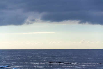 Obraz premium Breathtaking sunrise with sun hiding behind cloud, sea waves and blue sky with copy space