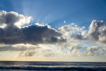Breathtaking sunrise with sun hiding behind cloud, sea waves and blue sky with copy space