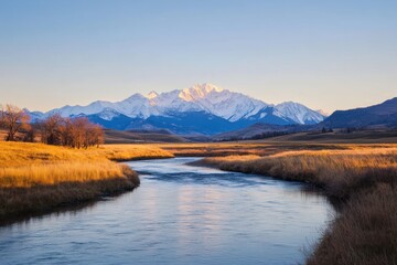 Fototapeta premium Serene River Flows Past Autumnal Grasslands Towards Snowy Mountains