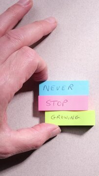 Positive personal growth mindset concept. Phrase Never Stop Growing handwritten on colourful sticky notes on grey textured paper background.