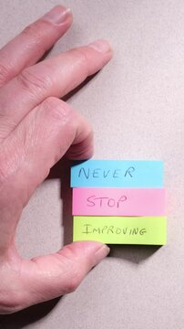 Personal development positive mindset concept. Phrase Never Stop Improving handwritten on colourful sticky notes on top of grey textured paper background.