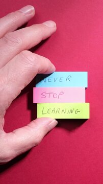 Never Stop Learning personal motivation, education mindset concept. Phrase Never Stop Learning written on colourful sticky notes on top of rich deep red paper background.