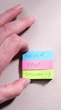 Positive mindset happiness concept. Words Never Stop Smiling handwritten on colourful sticky notes on top of textured grey paper background.