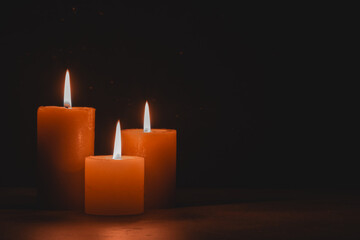 Burning candles on wooden table against background black wall.