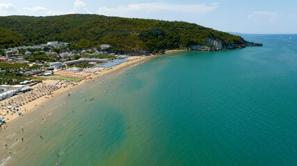 Obraz premium Aerial view of the beach of Peschici bay, in Puglia, Italy, on the coast of the Adriatic Sea. It's a tourist destination in Gargano, in the province of Foggia. There are many beach clubs and umbrellas