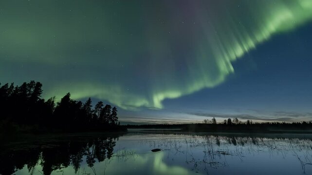Auroras starting to dance at dusk above a still lake