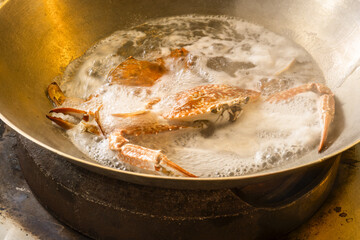 Fresh raw crab with blue claws cooking in a wok with a green pepper sauce, a specialty of Kep, Cambodia