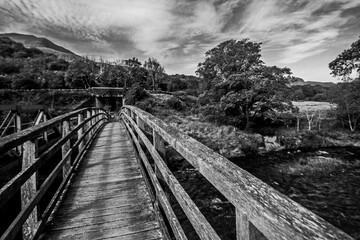 Dramatic Black and White view along a weathered Wooden Hiking bridge crossing the river Glaslyn in Eryri National Park in Wales. 