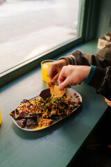 Two friends are enjoying a plate of nachos with guacamole, accompanied by glasses of orange juice